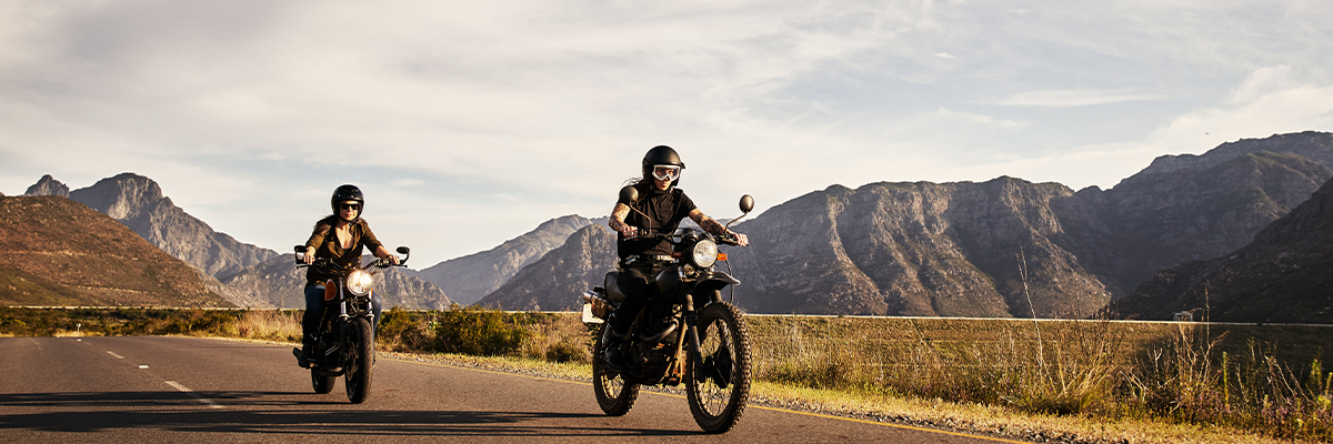 man and woman riding two seperate motorcylces through the mountians on a road
