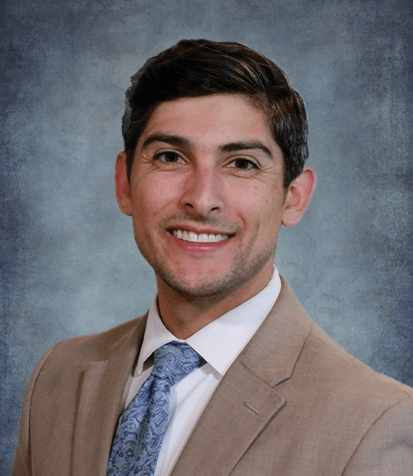 Spencer smiling at the camera wearing a tan suit and a blue tie