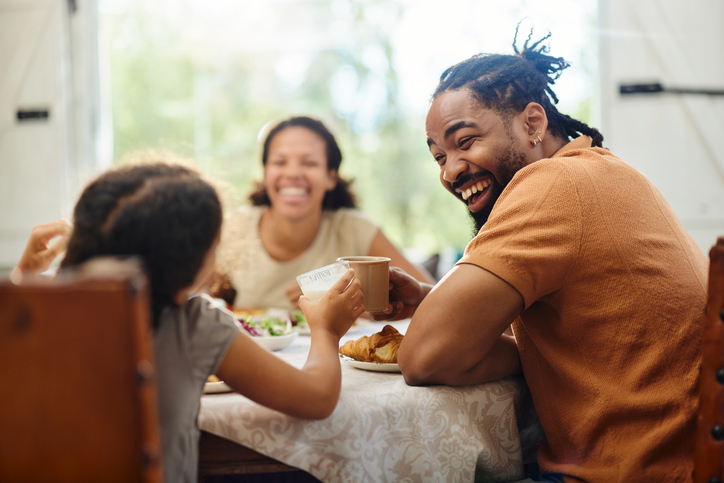 Family sitting at dinner table, dad and mom are smiling at their small child who's back is facing the camera