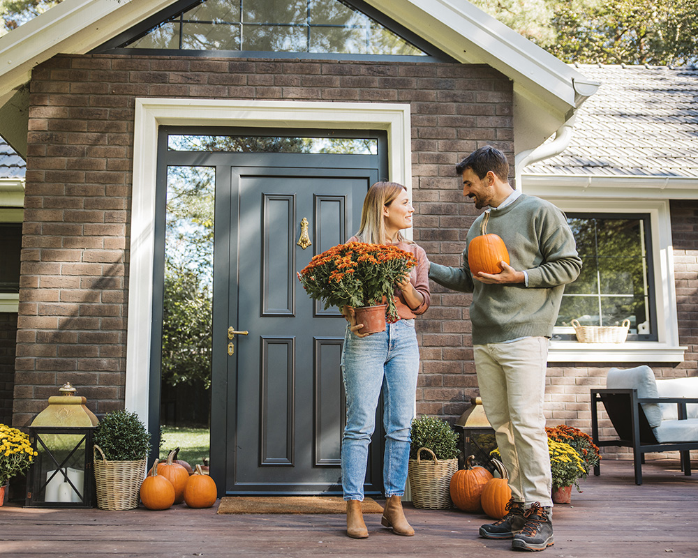 husband and wife putting pumpkins on their front porch