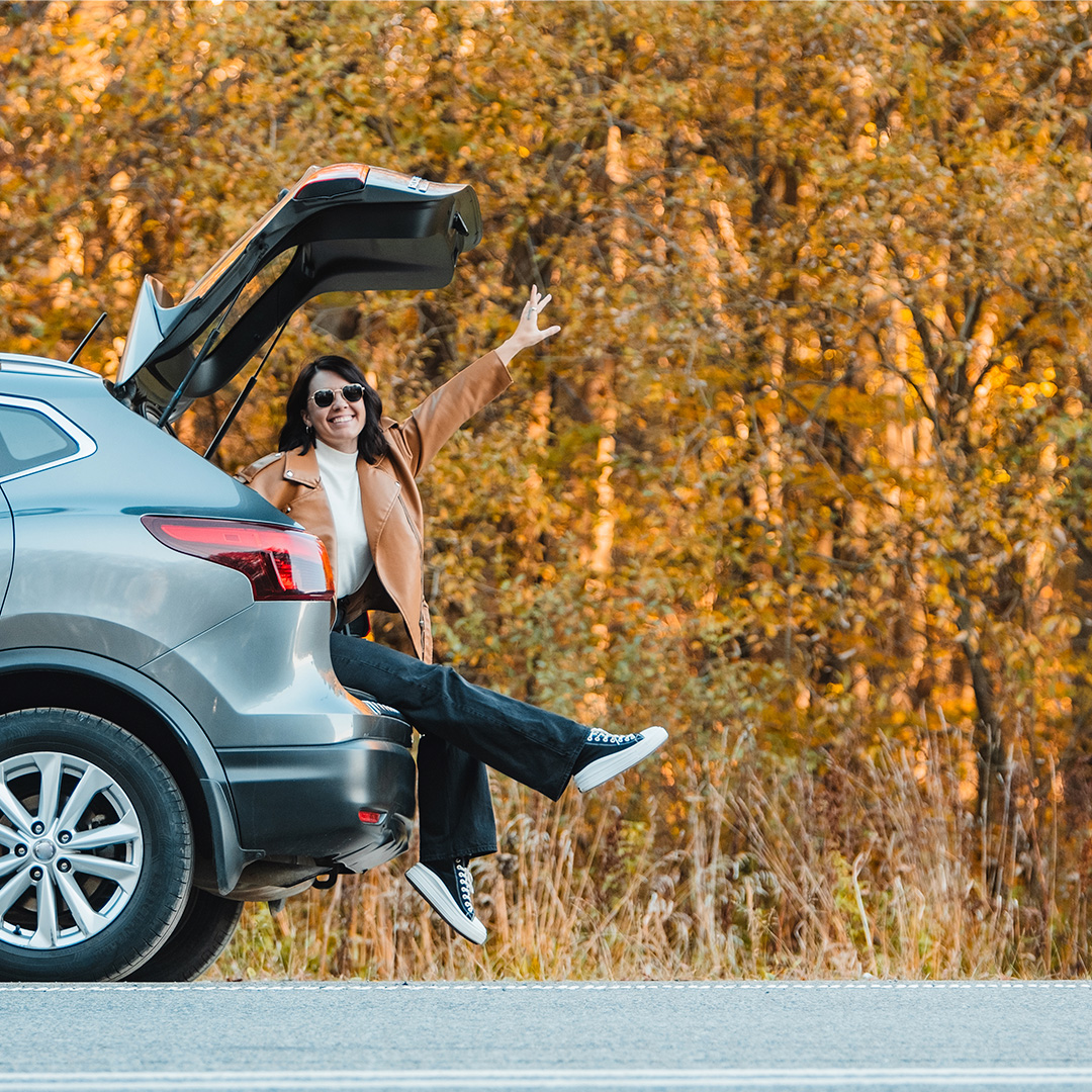 woman in the trunk of her car next to trees with orange leaves