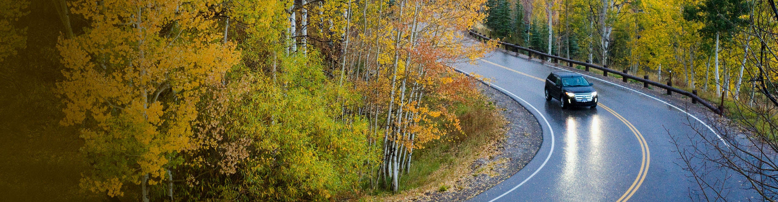 black car driving on a fall windy road