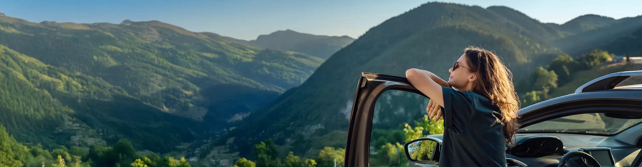 woman leaning on her car door staring at a mountain view